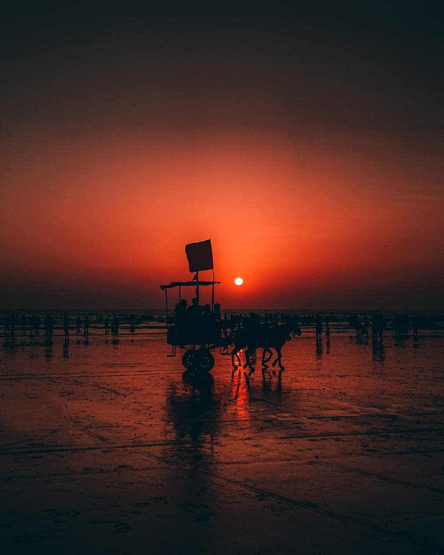 Horse-drawn carriage silhouetted against the setting sun on a wet beach