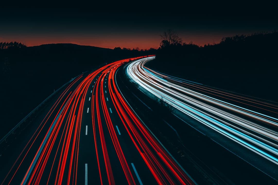 Long exposure of red and white light trails curving along a highway at dusk